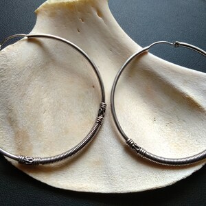 May include: A pair of silver hoop earrings with a coiled wire design. The earrings are large and have a simple, elegant look.