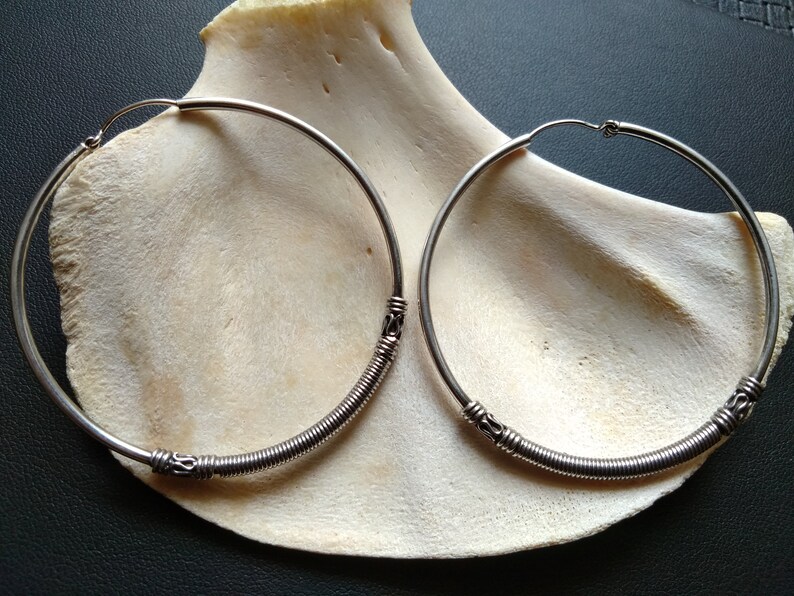 May include: A pair of silver hoop earrings with a coiled wire design. The earrings are large and have a simple, elegant look.