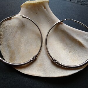 May include: Two silver hoop earrings with a coiled wire design. The earrings are large and have a simple, elegant look.
