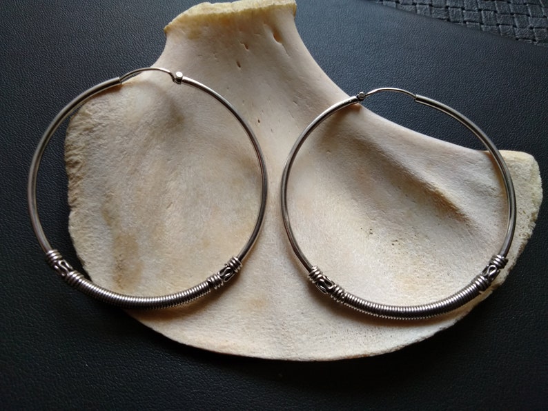 May include: Two silver hoop earrings with a coiled wire design. The earrings are large and have a simple, elegant look.