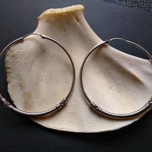 May include: A pair of silver hoop earrings with a twisted wire design. The earrings are large and have a simple, elegant look.