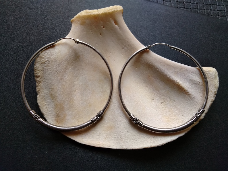 May include: A pair of silver hoop earrings with a twisted wire design. The earrings are large and have a simple, elegant look.