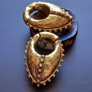 Może przedstawiać: Zestaw trzech ceramicznych kubków z nakrapianym, matowym wykończeniem. Kubki są w odcieniach kremu, jasnoszarym i ciemnoszarym. Każdy kubek ma prosty, minimalistyczny design.