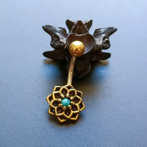 May include: A gold belly button ring with a turquoise gemstone in the center of a flower design.