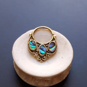 Op de afbeelding: Goudkleurige metalen hanger met drie ovale, iriserende inlays. De hanger heeft een cirkelvormig ontwerp met decoratieve filigraanelementen. De iriserende inlays tonen tinten blauw, groen en paars.