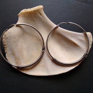May include: A pair of silver hoop earrings with a twisted wire design. The earrings are on a white background.
