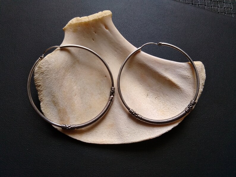 May include: A pair of silver hoop earrings with a twisted wire design. The earrings are on a white background.