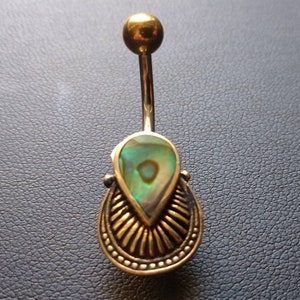 Puede incluir: Anillo de ombligo dorado con una concha de abulón en forma de lágrima. La concha tiene colores verde, azul e iridiscente.