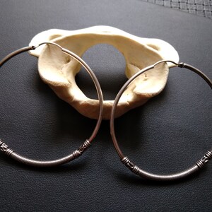 May include: Two silver hoop earrings with a twisted wire design. The earrings are on a black surface.