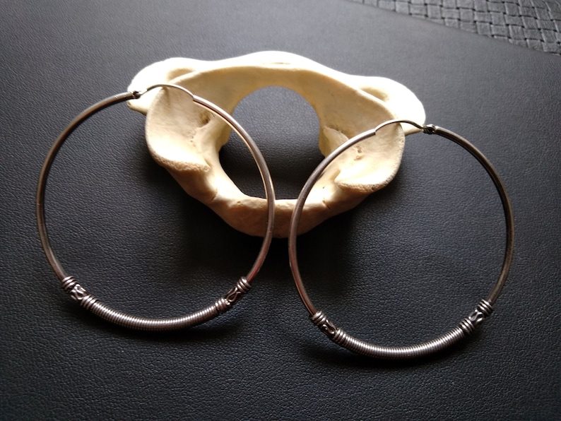 May include: Two silver hoop earrings with a twisted wire design. The earrings are on a black surface.