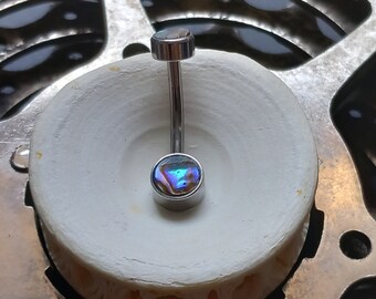 May include: A silver belly button ring with a colorful, iridescent abalone shell-like stone on the bottom and a smaller, matching stone on top. The jewelry is set against a white, circular background.
