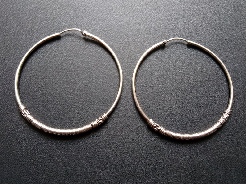 May include: A pair of silver hoop earrings with a textured design. The hoops are large and circular.