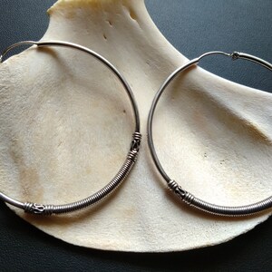 May include: A pair of silver hoop earrings with a twisted wire design. The earrings are displayed on a white shell.