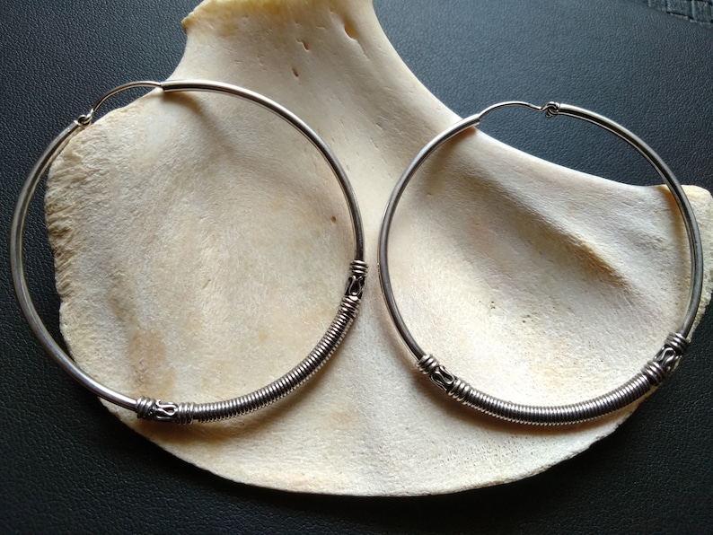 May include: A pair of silver hoop earrings with a twisted wire design. The earrings are displayed on a white shell.