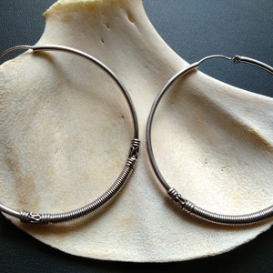 May include: A pair of silver hoop earrings with a coiled wire design. The earrings are large and have a simple, elegant look.