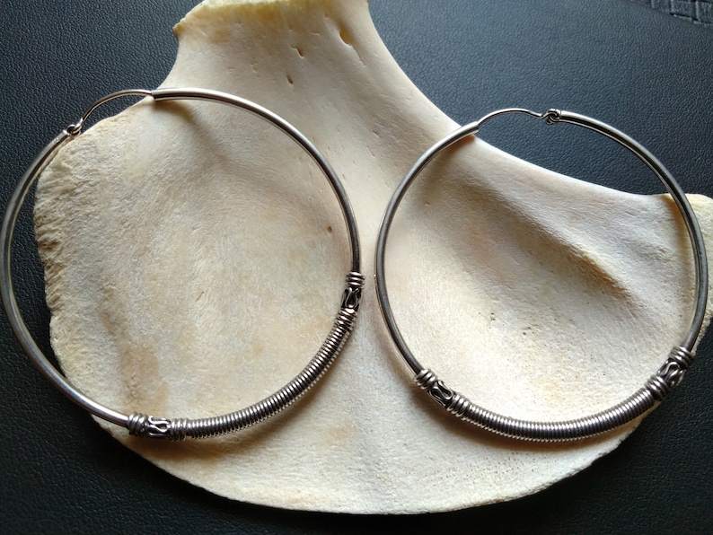 May include: A pair of silver hoop earrings with a coiled wire design. The earrings are large and have a simple, elegant look.