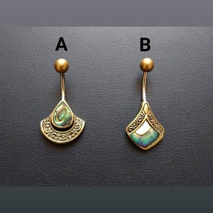 Peut inclure: Deux piercings de nombril en métal doré avec des incrustations d'ormeau irisé. L'un est en forme de goutte d'eau avec une bordure décorative, l'autre en forme de losange. Les deux ont une petite boule dorée au sommet.