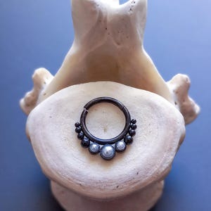 Peut inclure: Boucle d'oreille en forme de cercle noir avec une rangée de perles noires et trois perles blanches.