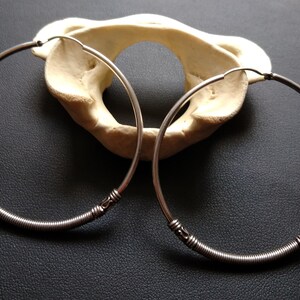 May include: A pair of silver hoop earrings with a coiled wire design and decorative accents. The earrings are displayed on a white surface.