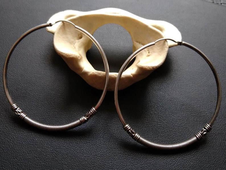 May include: A pair of silver hoop earrings with a coiled wire design and decorative accents. The earrings are displayed on a white surface.