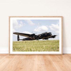 Könnte beinhalten: Gerahmter Druck eines schwarzen und gelben Oldtimer-Flugzeugs auf einem grasbewachsenen Feld unter einem bewölkten Himmel. Das Flugzeug hat große Flügel und Propeller. Das Bild ist in einem Holzrahmen.