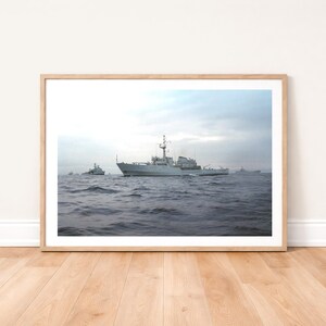Könnte beinhalten: Ein gerahmter Druck mit mehreren Militärschiffen, die auf einem Gewässer unter einem bewölkten Himmel segeln. Die Schiffe sind hellgrau und das Wasser ist dunkelblau. Der Druck wird auf einem Holzboden präsentiert.