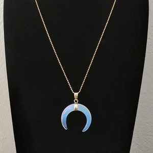 K&ouml;nnte beinhalten: Eine goldene Kettenkette mit einem Halbmond-Anh&auml;nger aus irisierendem Opal.
