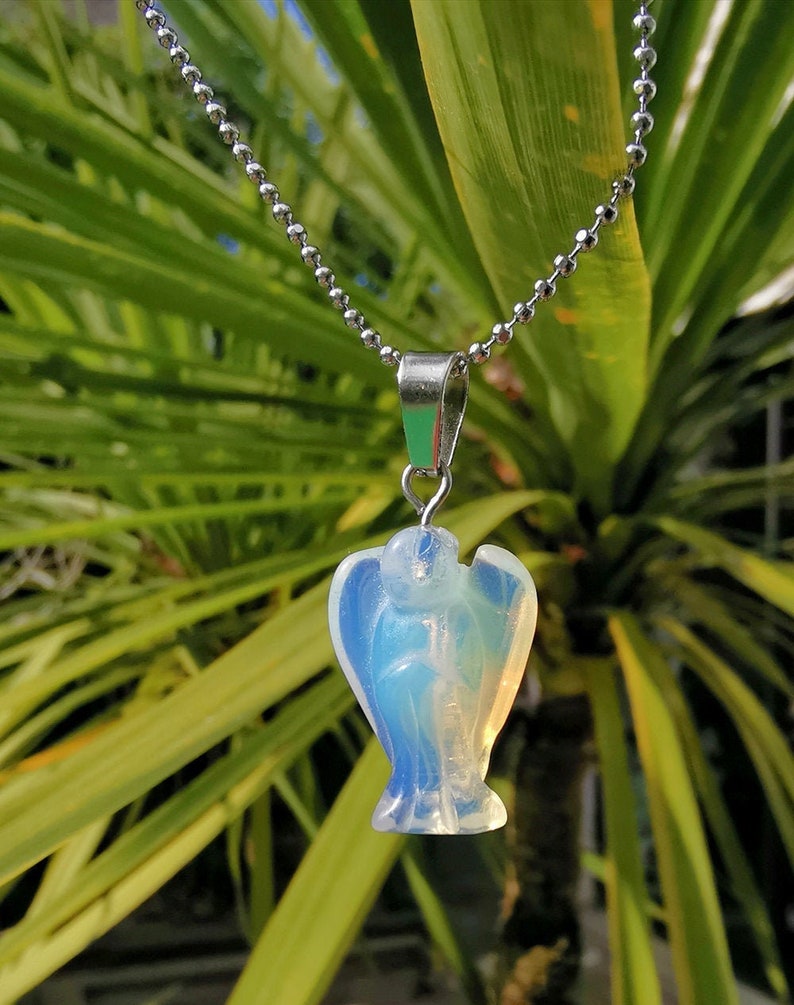 Op de afbeelding: Een zilveren ketting met een heldere, iriserende engelhanger. De engel is gegraveerd uit een doorschijnende steen en heeft een delicaat, vrouwelijk ontwerp.