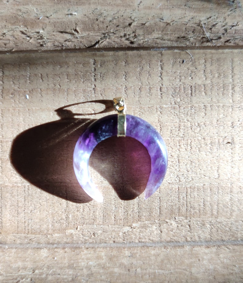 K&ouml;nnte beinhalten: Ein Halbmond-Anh&auml;nger aus Amethyst mit einer goldfarbenen &Ouml;se. Der Amethyst ist tiefviolett mit wei&szlig;en Streifen.