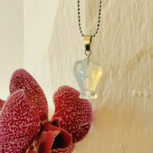 Op de afbeelding: Een zilveren ketting met een hartvormige hanger van opaal. De opaal is iriserend en heeft een melkachtig witte kleur.