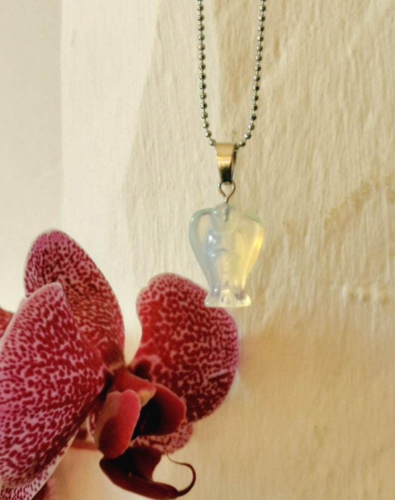 Op de afbeelding: Een zilveren ketting met een hartvormige hanger van opaal. De opaal is iriserend en heeft een melkachtig witte kleur.
