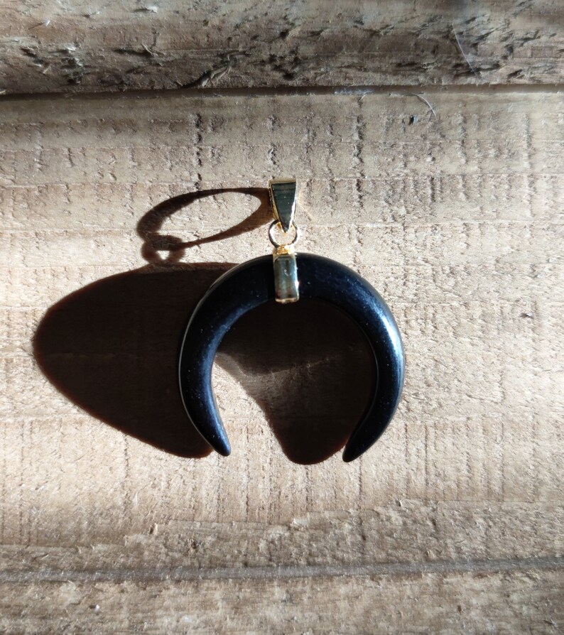 K&ouml;nnte beinhalten: Ein schwarzer Halbmond-Anh&auml;nger mit einer goldenen &Ouml;se. Der Anh&auml;nger ist aus Holz und hat eine glatte, polierte Oberfl&auml;che.