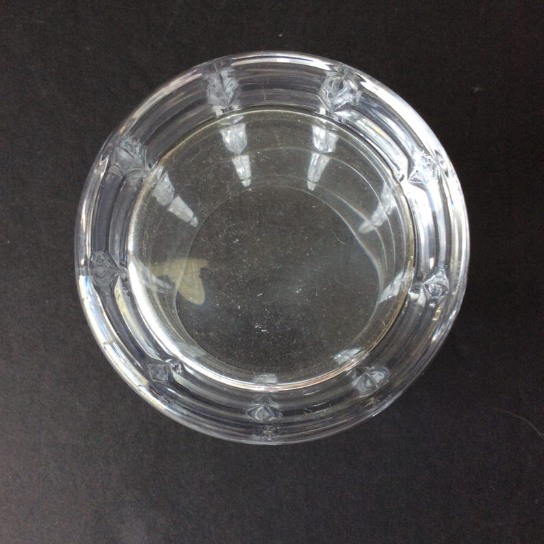 Op de afbeelding: Een ronde kom van helder glas met een gladde binnenkant en een dikke, getextureerde buitenrand. De rand is versierd met een herhalend patroon van kleine, verhoogde geometrische inkepingen die zorgen voor een gefacetteerd uiterlijk rondom.