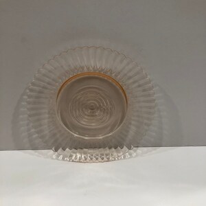 Puede incluir: Un plato de cristal transparente te&ntilde;ido de rosa, con borde festoneado. El plato tiene un dise&ntilde;o acanalado que irradia desde el centro, con un borde dorado. El plato es probablemente vintage o antiguo, adecuado para servir o exhibir.