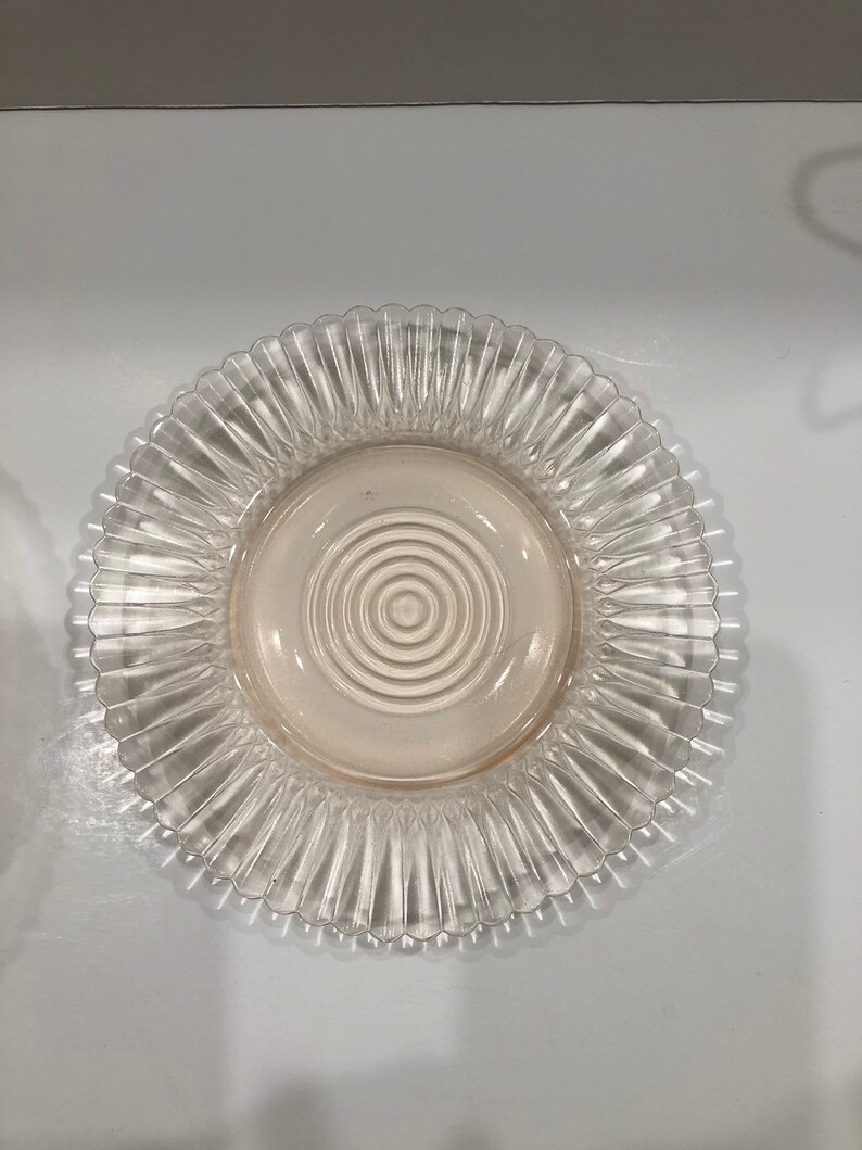 Puede incluir: Plato de vidrio transparente con borde acanalado y zona central con c&iacute;rculos conc&eacute;ntricos. El plato tiene un ligero tono rosado en el centro. Ideal para servir alimentos.