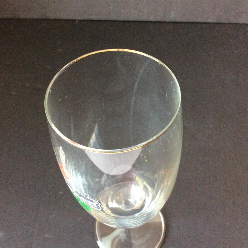 May include: A clear, stemmed glass with a gold rim. The glass has a wide, rounded bowl and a slender stem. The glass is empty and appears to be clean. The glass is likely used for serving beverages.