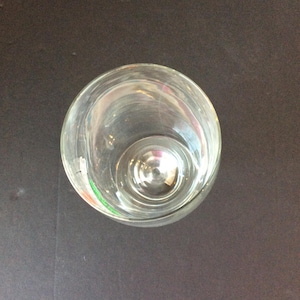 May include: A clear, empty glass with a rounded bowl and a short stem. The glass is made of transparent material, allowing a view through its interior. The image is taken from a top-down perspective, showcasing the glass's circular shape.