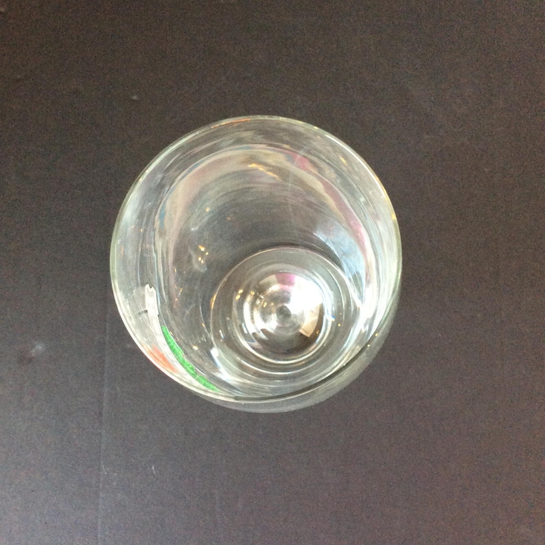May include: A clear, empty glass with a rounded bowl and a short stem. The glass is made of transparent material, allowing a view through its interior. The image is taken from a top-down perspective, showcasing the glass's circular shape.