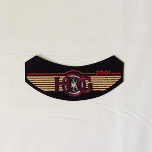 May include: Black embroidered patch with the letters "HOG" in a stylized font, a wheel design, and the year "2001". The patch has a curved shape with tan and red accents, and a black background.