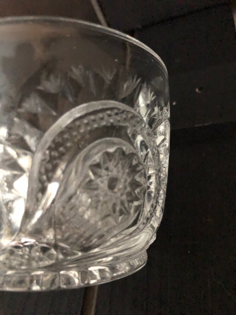 May include: Clear glass bowl with intricate cut glass patterns. The bowl features a starburst design at the base and diamond-shaped cuts around the sides. The rim is smooth, and the bowl appears to be vintage or antique.
