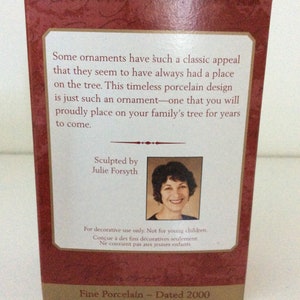 May include: A maroon box with text about a porcelain ornament. The text reads "Some ornaments have such a classic appeal...Sculpted by Julie Forsyth...Fine Porcelain - Dated 2000". A photo of Julie Forsyth is included.