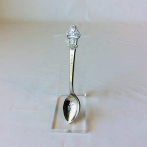 May include: A silver spoon with the word "LUCERNE" engraved on the handle. The spoon's top features the Rolex logo. The spoon is displayed on a clear acrylic stand.