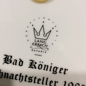 以下が含まれることがあります： 白磁のプレートに、黒と白のロゴが描かれており、「Lang Ebrach Bavaria Germany」と王冠が書かれています。 「Bad K&ouml;niger Weihnachtsteller 1983」というテキストが黒で書かれています。