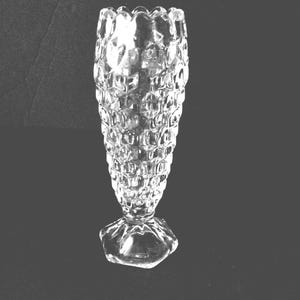 Pode incluir: Um vaso de vidro transparente com um padrão texturizado em forma de favo de mel. O vaso tem uma borda alargada e ondulada e assenta numa base hexagonal. O vaso tem aproximadamente 15 cm de altura.