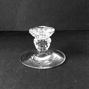 Op de afbeelding: Glazen kandelaar met een ronde voet en een facetgeslepen, decoratieve steel. De bovenkant heeft een cirkelvormige inkeping om een kaars in te plaatsen. De kandelaar is ongeveer 13 cm hoog.