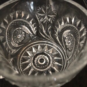 May include: Clear glass bowl with intricate starburst and swirl patterns. The bowl's design features detailed cuts and shapes, creating a textured surface. The bowl's rim is visible, and the overall aesthetic is vintage.