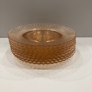 Puede incluir: Una pila de platos de vidrio de color naranja claro. Cada plato tiene un borde festoneado y un dise&ntilde;o en espiral en el centro. Los platos est&aacute;n apilados ordenadamente uno encima del otro, creando una disposici&oacute;n visualmente atractiva.