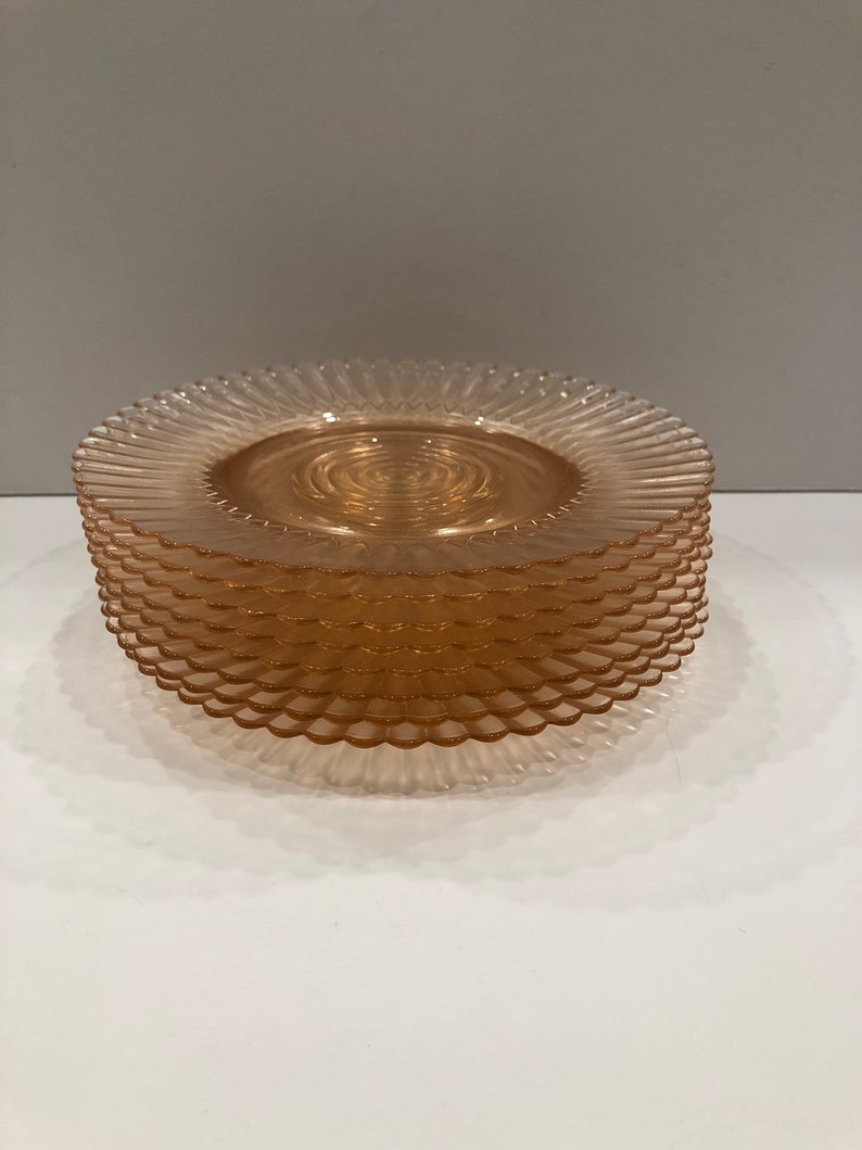 Puede incluir: Una pila de platos de vidrio de color naranja claro. Cada plato tiene un borde festoneado y un dise&ntilde;o en espiral en el centro. Los platos est&aacute;n apilados ordenadamente uno encima del otro, creando una disposici&oacute;n visualmente atractiva.