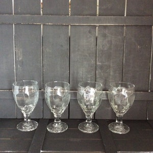 May include: Four clear glass goblets with a textured design sit on a black wooden surface.