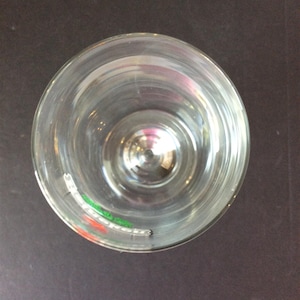 May include: A clear, empty glass with a wide rim, viewed from above. The glass is circular and sits on a dark surface. The glass has a slight reflection and a small amount of color at the bottom.